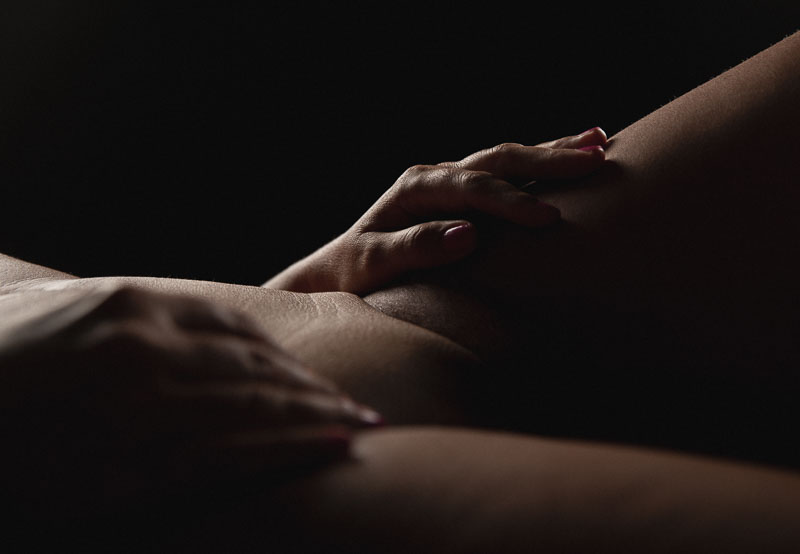 Lähikuva naisen kädestä reidellä alastoman häpykummun vieressä kriittisten paikkojen jäädessä varjon sensuroimaksi